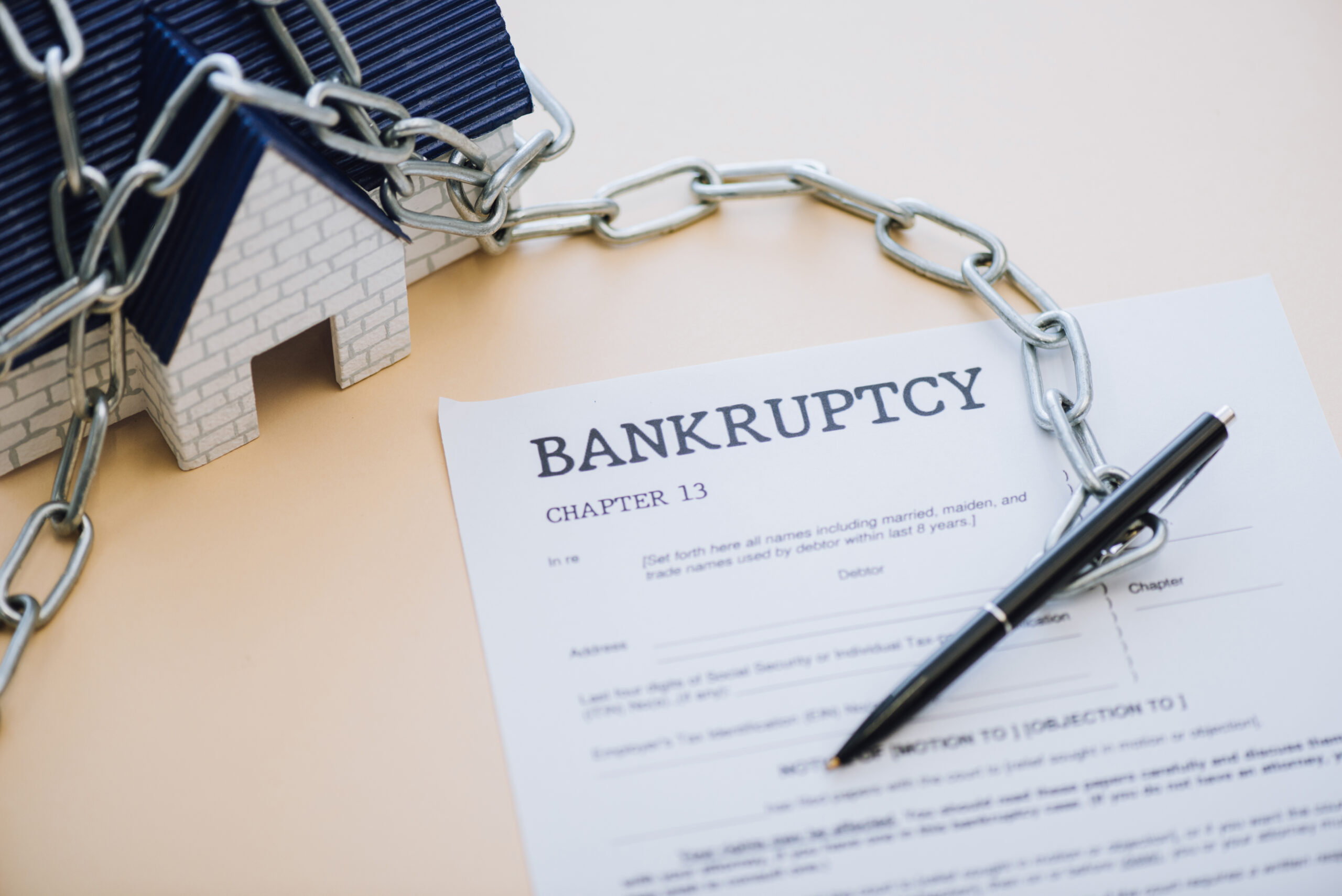High angle view of house model with chain near pen and document with bankruptcy and chapter 13 lettering on beige