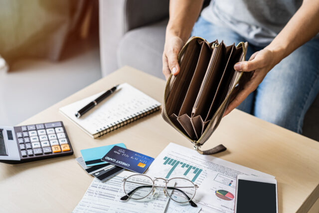 Stressed young woman open her empty wallet and calculating expenses at home