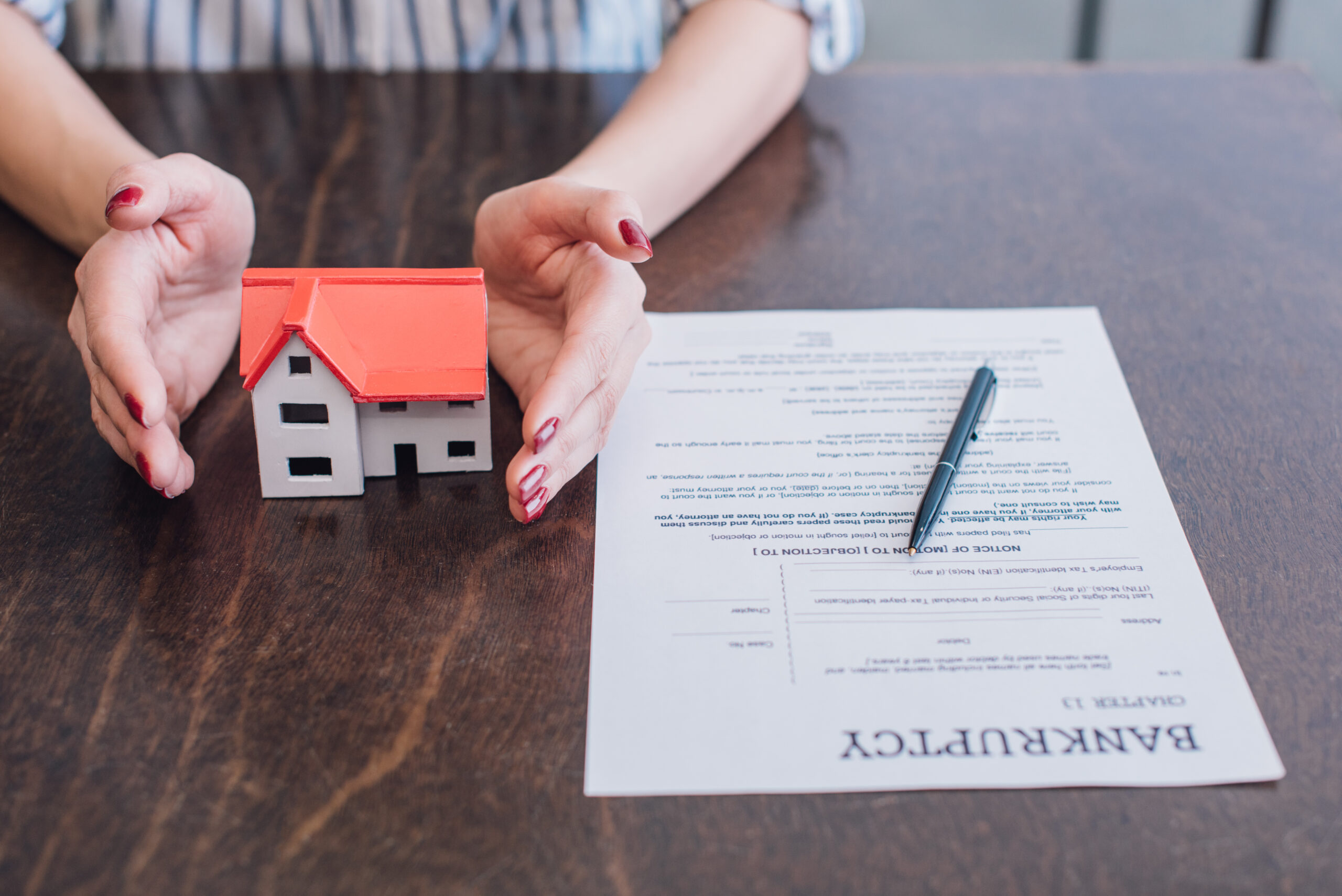 Partial view of female hands near house model, paper with bankruptcy lettering and pen on table