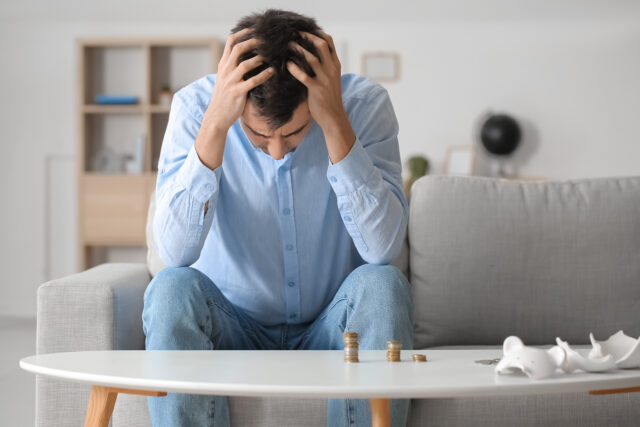 Stressed man with coins at home. Bankruptcy concept