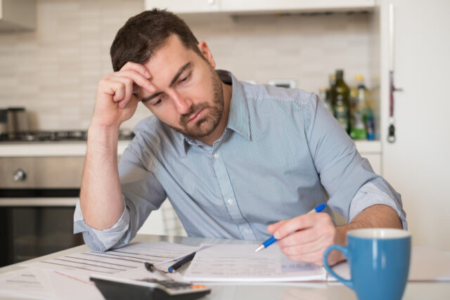 Frustrated man calculating bills and tax expenses.