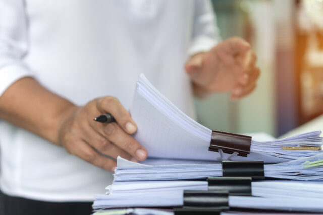 Employee woman hands checking Business unfinished Documents with stacks paper files and searching document achieves preparing meeting planing at busy work desk office